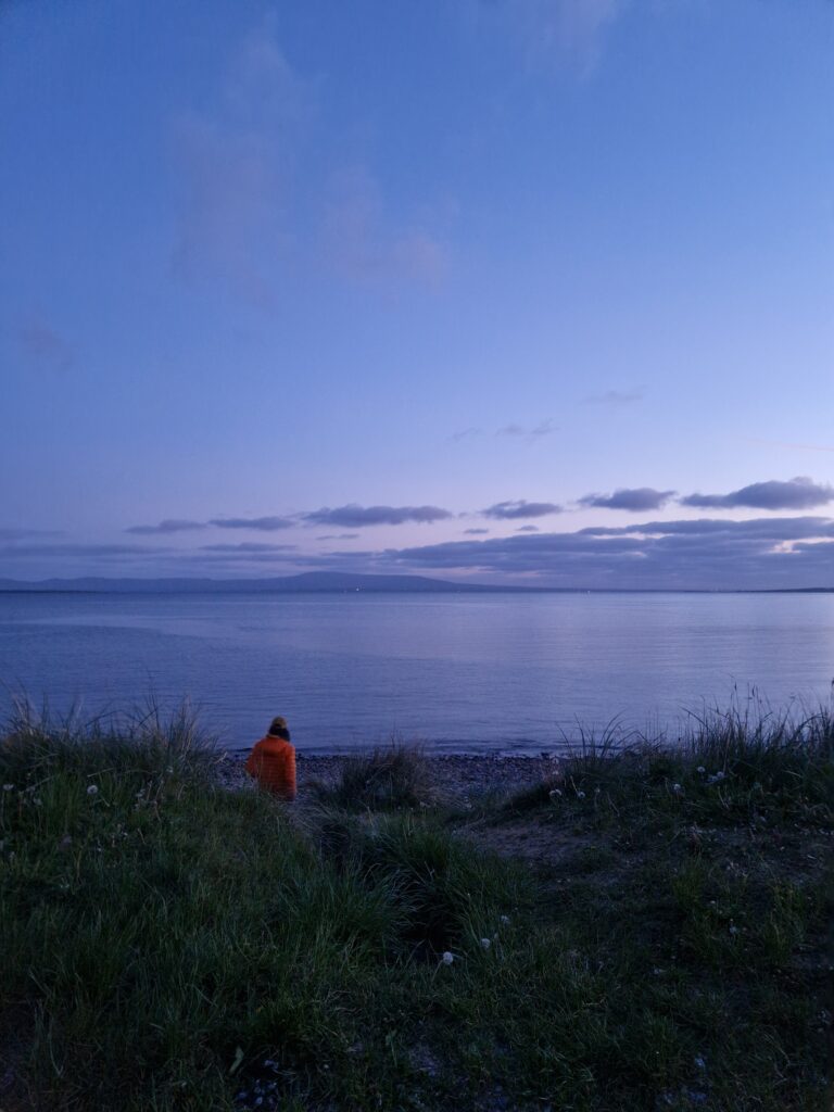 Vyras, vaikštantis Airijos paplūdimyje, leidžiantis saulei