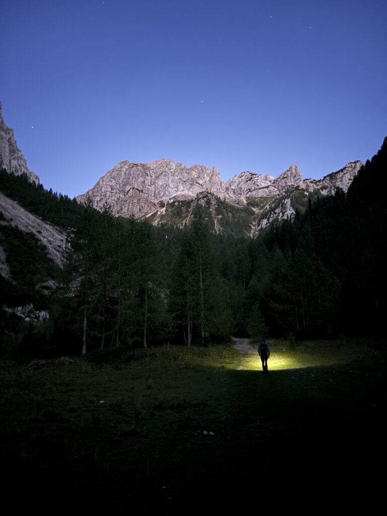 Žmogus besišviečiantis sau taką tamsoje su kalnų siluetu tolumoje